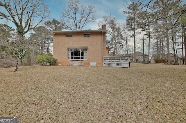 rear view of property featuring a yard, a chimney, a deck, and brick siding