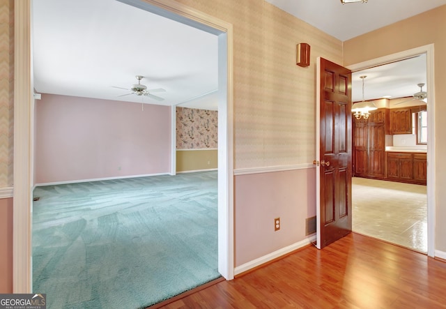 hallway featuring wallpapered walls, visible vents, baseboards, wood finished floors, and carpet