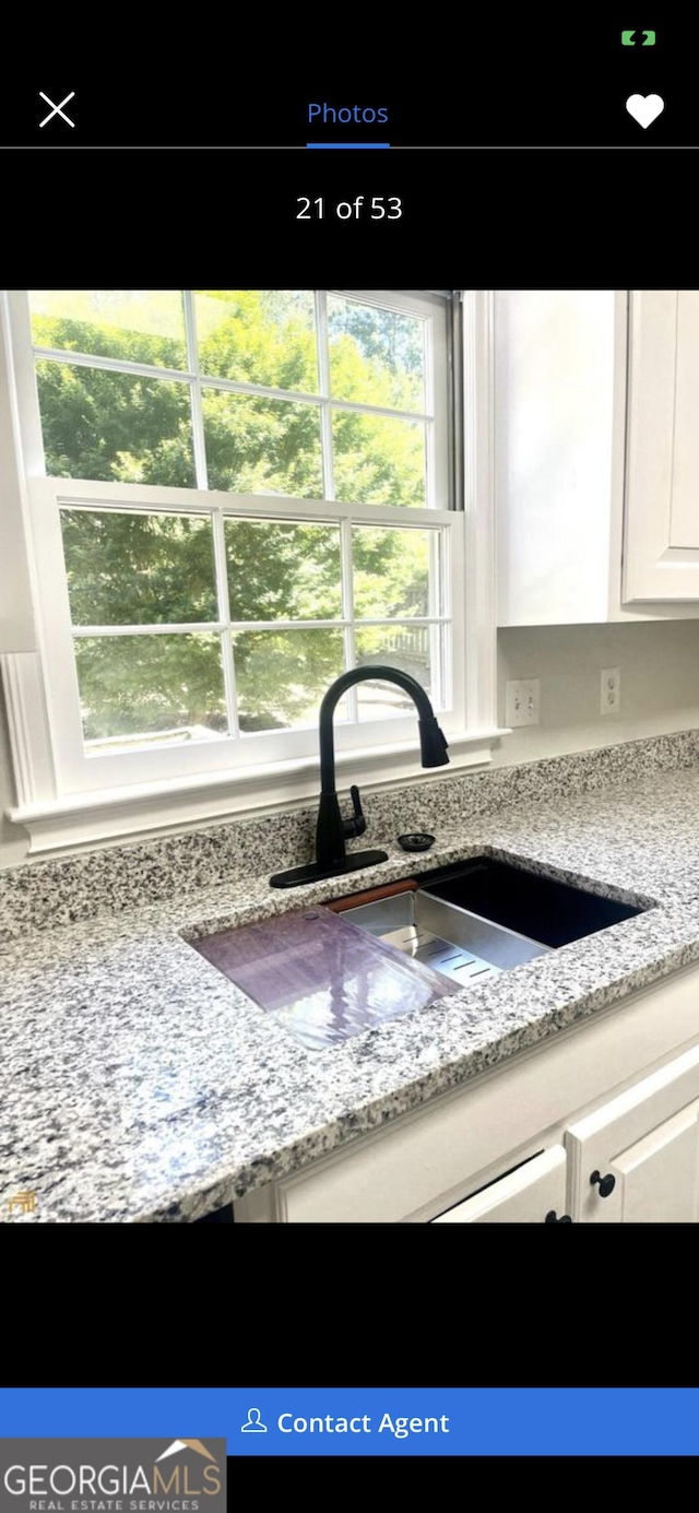 interior details featuring light stone counters, a sink, and white cabinetry