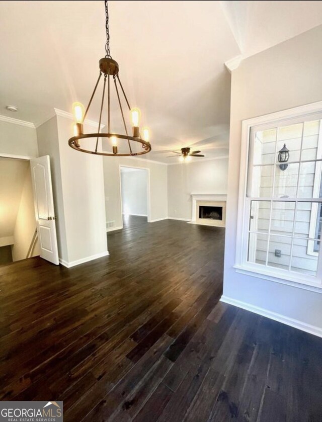 unfurnished living room with dark wood finished floors, a fireplace, ornamental molding, baseboards, and ceiling fan with notable chandelier