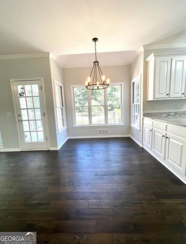 unfurnished dining area with a notable chandelier, visible vents, baseboards, ornamental molding, and dark wood finished floors