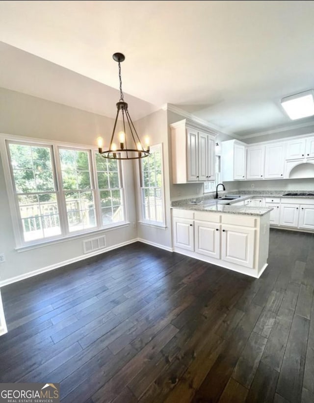 kitchen with light stone counters, visible vents, hanging light fixtures, white cabinetry, and a sink