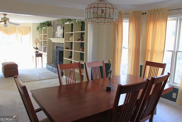 dining space with carpet floors, ceiling fan, ornamental molding, and a fireplace with raised hearth