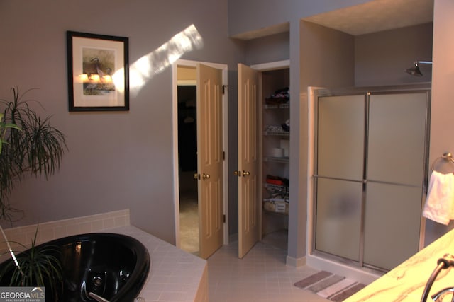 bathroom with a shower stall, a tub with jets, a walk in closet, and tile patterned floors