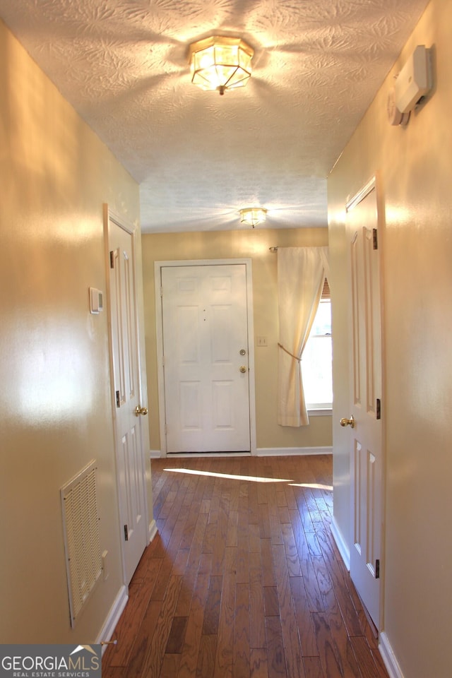 hallway with dark wood-style floors, visible vents, a textured ceiling, and baseboards