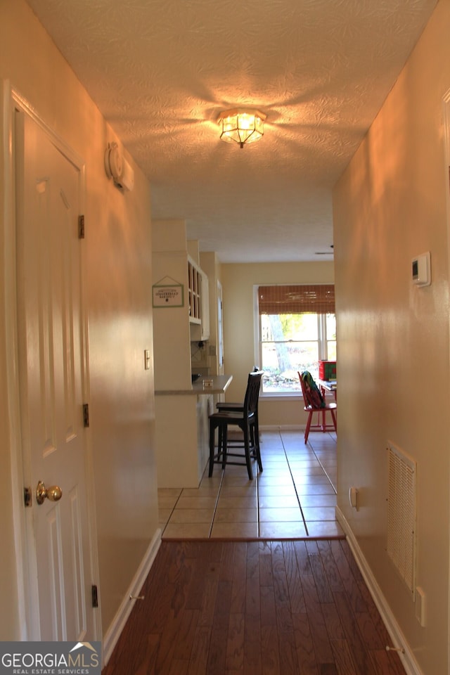 corridor with a textured ceiling, hardwood / wood-style floors, visible vents, and baseboards