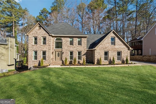 view of front of property with brick siding, a front lawn, and roof with shingles