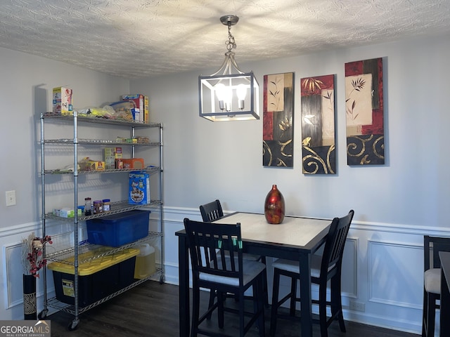 dining space with dark wood-type flooring, a textured ceiling, and wainscoting