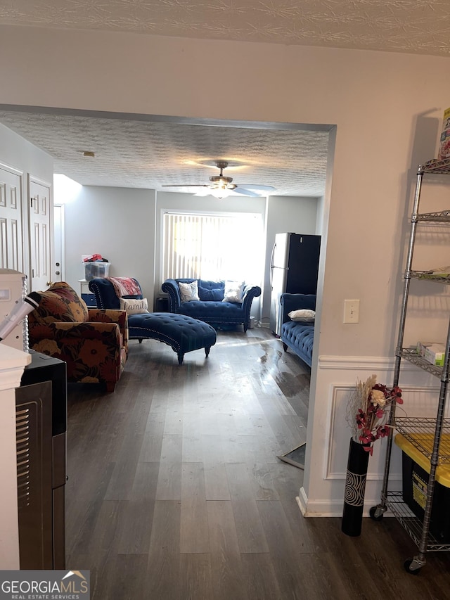 living area featuring a textured ceiling, dark wood finished floors, and a ceiling fan