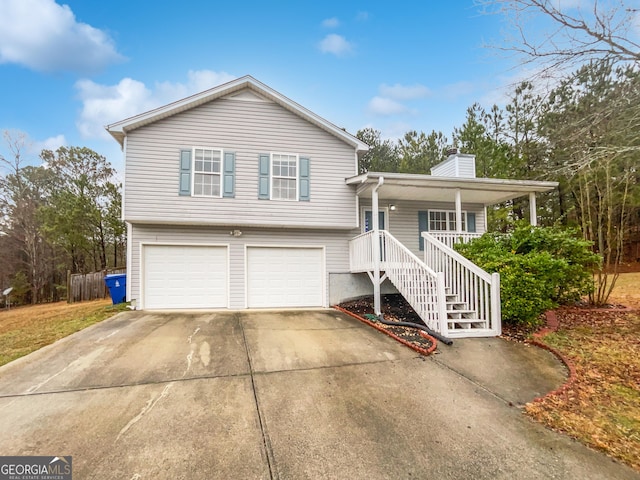 split level home featuring a chimney, a porch, concrete driveway, stairway, and an attached garage