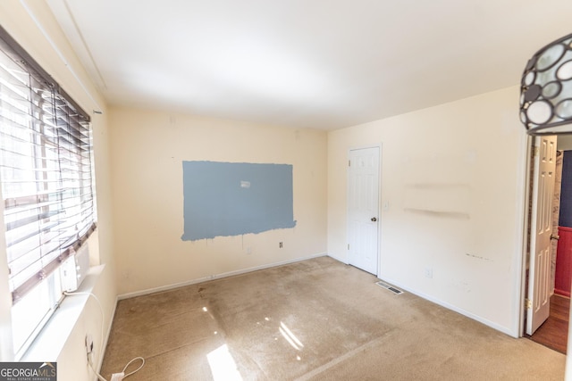 empty room featuring light colored carpet, visible vents, and baseboards