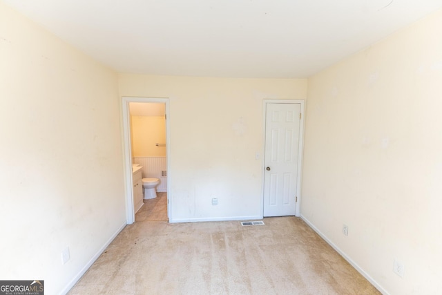 unfurnished bedroom featuring baseboards, visible vents, connected bathroom, and light colored carpet