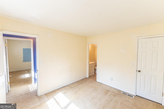 unfurnished bedroom with baseboards, ensuite bathroom, visible vents, and light colored carpet