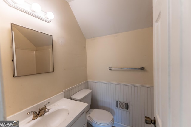 bathroom featuring visible vents, wainscoting, toilet, vaulted ceiling, and vanity