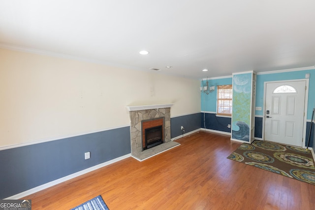 entrance foyer featuring crown molding, a notable chandelier, a fireplace, wood finished floors, and baseboards