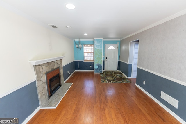 entryway featuring a stone fireplace, wood finished floors, visible vents, baseboards, and crown molding