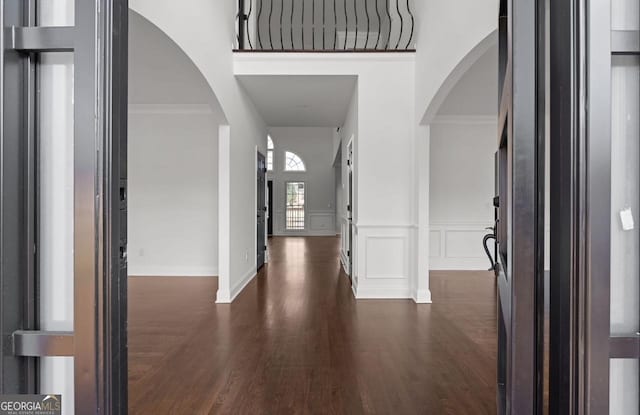 entrance foyer with arched walkways, dark wood-style flooring, and a decorative wall