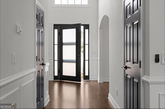 entrance foyer featuring arched walkways, dark wood finished floors, a towering ceiling, and a decorative wall