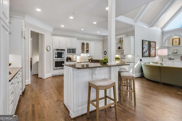 kitchen with white cabinets, open floor plan, appliances with stainless steel finishes, dark stone countertops, and glass insert cabinets