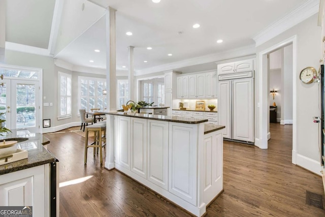 kitchen with dark wood-style floors, paneled built in refrigerator, white cabinets, and dark stone countertops