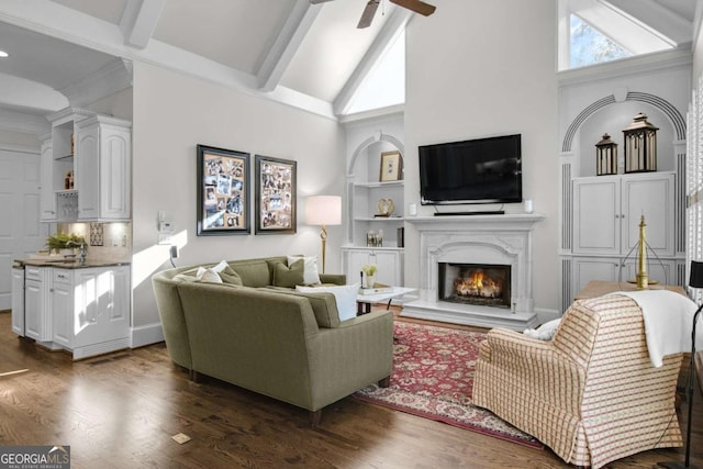 living area featuring dark wood-style floors, a fireplace, beam ceiling, and a ceiling fan