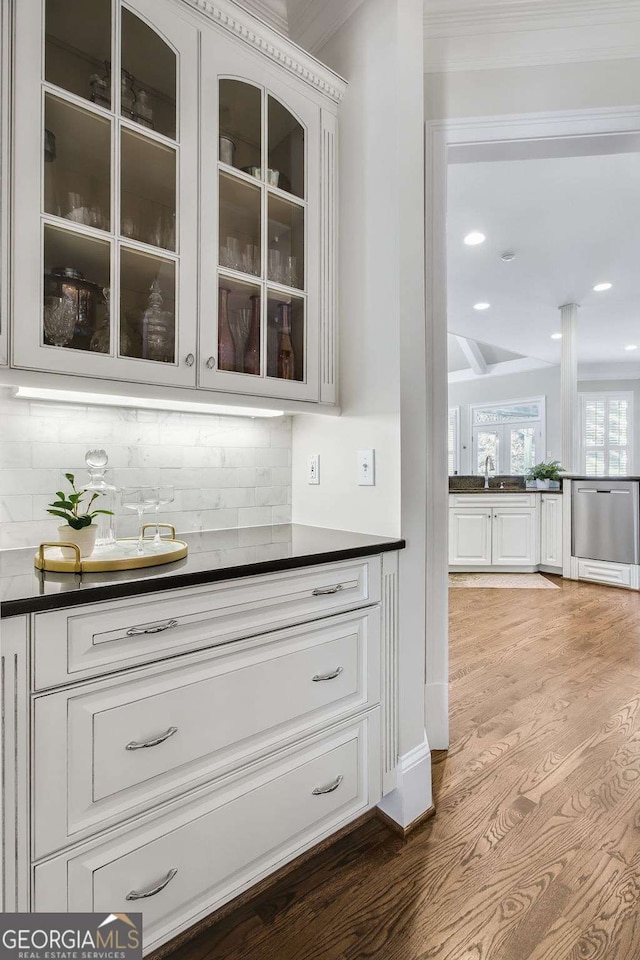 bar featuring decorative backsplash, wood finished floors, stainless steel dishwasher, a sink, and recessed lighting