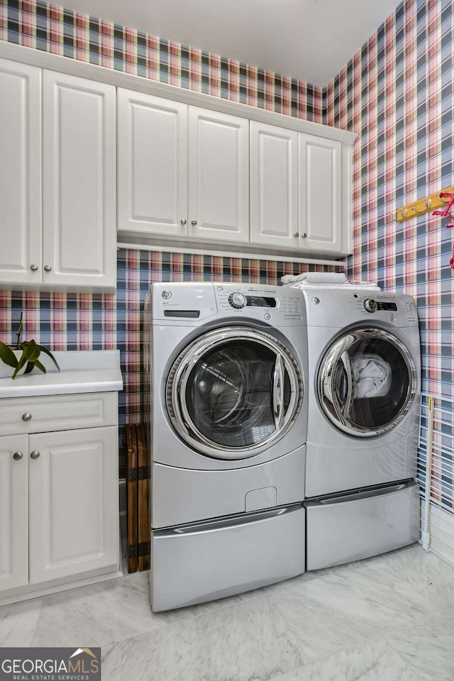 clothes washing area featuring cabinet space, washing machine and clothes dryer, and wallpapered walls