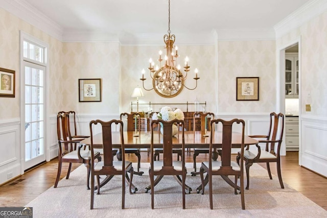 dining room with light wood-type flooring, ornamental molding, a chandelier, and wainscoting