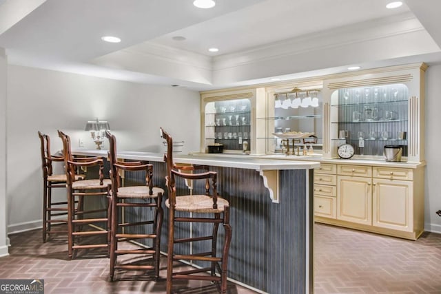 bar featuring a bar, brick floor, ornamental molding, and a tray ceiling