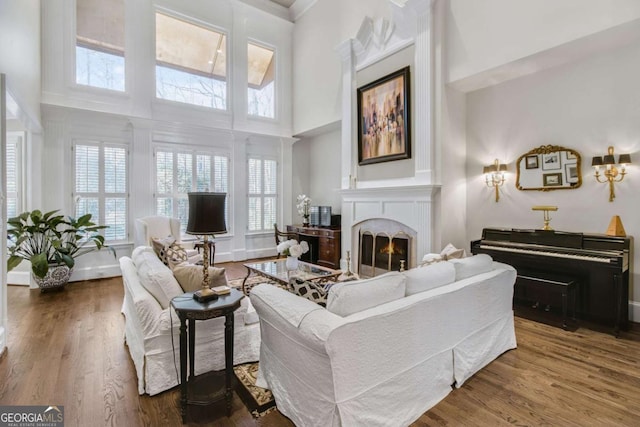 living room featuring baseboards, a lit fireplace, a towering ceiling, and wood finished floors