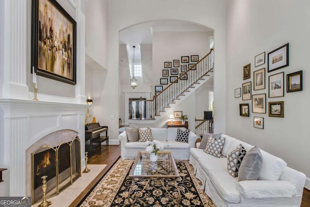 living room featuring a high ceiling, wood finished floors, a fireplace with flush hearth, baseboards, and stairs