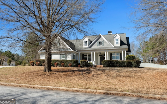 cape cod home with covered porch, a chimney, and fence