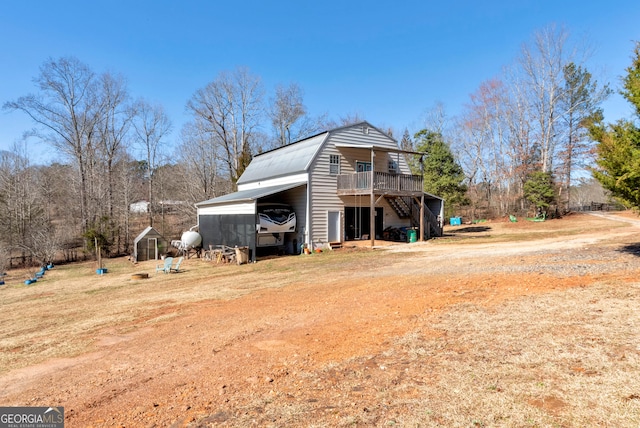 exterior space featuring a gambrel roof, dirt driveway, stairway, a wooden deck, and a carport