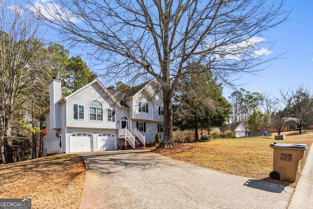 split foyer home featuring driveway, a garage, a chimney, and a front lawn