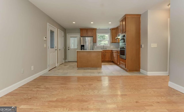 kitchen with brown cabinetry, a center island, stainless steel appliances, light countertops, and light wood-style floors