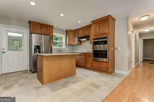 kitchen featuring stainless steel appliances, light countertops, brown cabinetry, a kitchen island, and under cabinet range hood