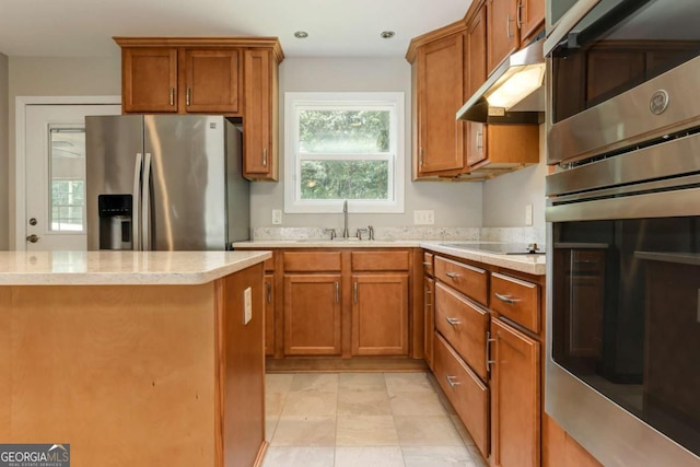 kitchen featuring a sink, appliances with stainless steel finishes, brown cabinets, and under cabinet range hood