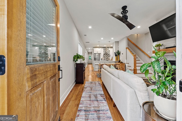 living area featuring light wood finished floors, baseboards, ceiling fan, stairway, and recessed lighting