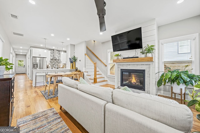 living room featuring light wood-type flooring, visible vents, stairway, and a tile fireplace