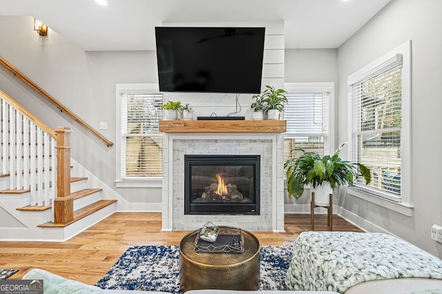 living area with a tile fireplace, stairway, baseboards, and wood finished floors