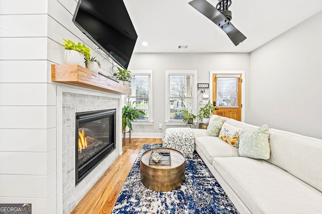 living area featuring visible vents, baseboards, a glass covered fireplace, light wood-style flooring, and ceiling fan