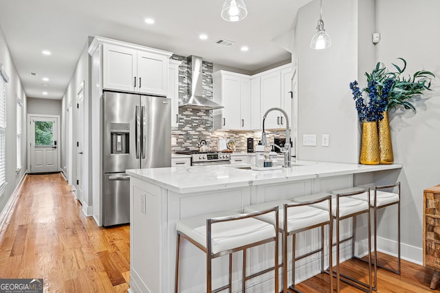 kitchen with a peninsula, visible vents, white cabinets, appliances with stainless steel finishes, and wall chimney exhaust hood