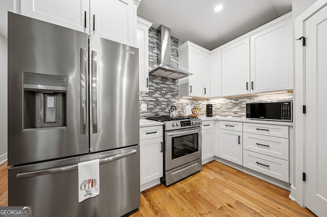 kitchen with decorative backsplash, appliances with stainless steel finishes, light wood-style floors, white cabinetry, and wall chimney range hood