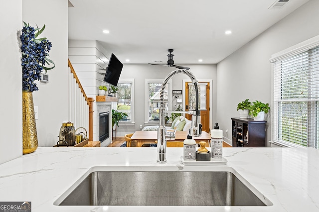 details featuring visible vents, a glass covered fireplace, light stone counters, a sink, and recessed lighting