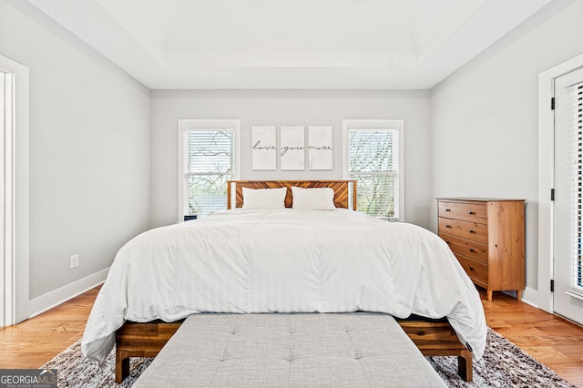 bedroom featuring multiple windows, a tray ceiling, and wood finished floors