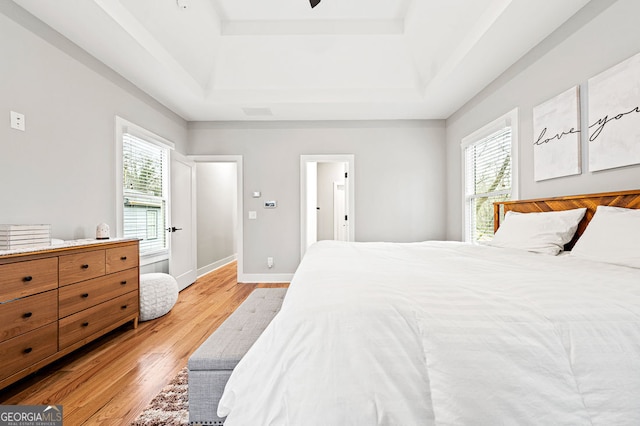 bedroom with light wood finished floors, a tray ceiling, multiple windows, and baseboards