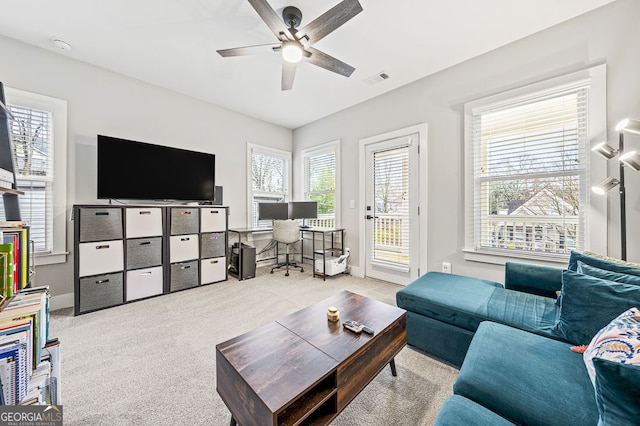 living area featuring baseboards, visible vents, a ceiling fan, and light colored carpet