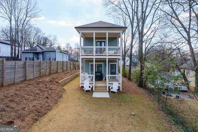 back of property featuring roof with shingles, covered porch, a lawn, a balcony, and a fenced backyard