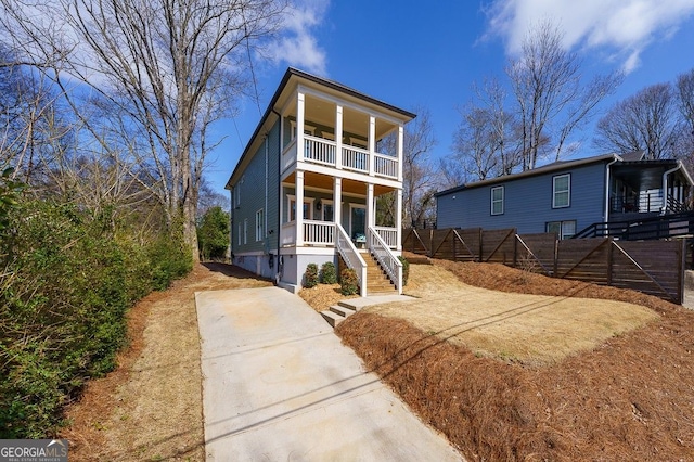 view of front of property with stairway, covered porch, fence, and a balcony