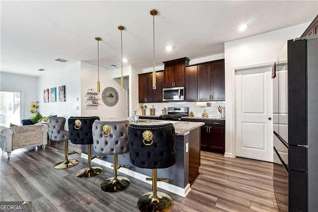 kitchen featuring a breakfast bar area, dark brown cabinetry, visible vents, open floor plan, and appliances with stainless steel finishes